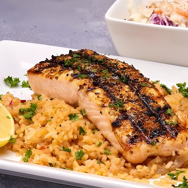 Grilled salmon with rice pilaf and a lemon wedge, served with a side of coleslaw.