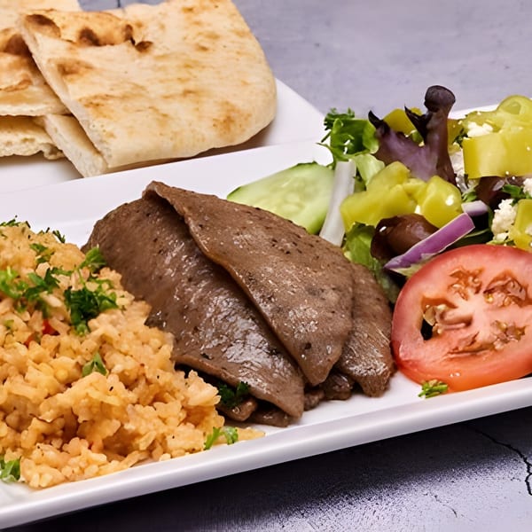 A gyro platter with sliced meat, rice, Greek salad, and pita bread on a white plate.