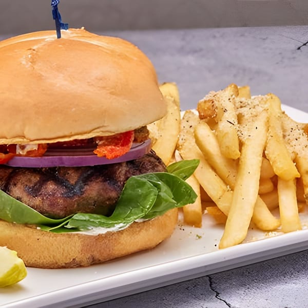 Gourmet burger with lettuce, onion, tomato, and a side of seasoned fries and a pickle spear.